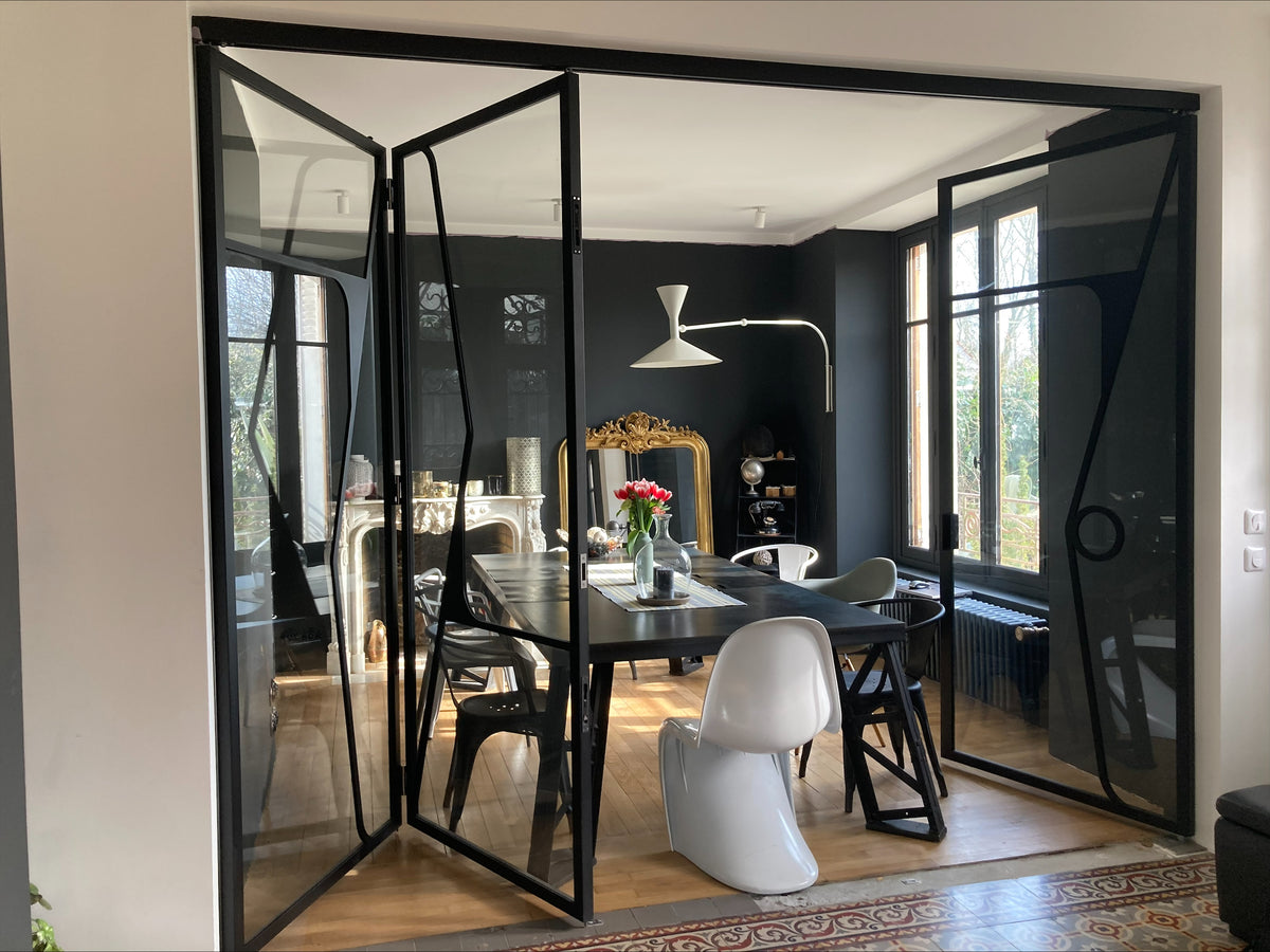 Verrière noire aux portes ouvertes sur une salle à manger aux murs sombres